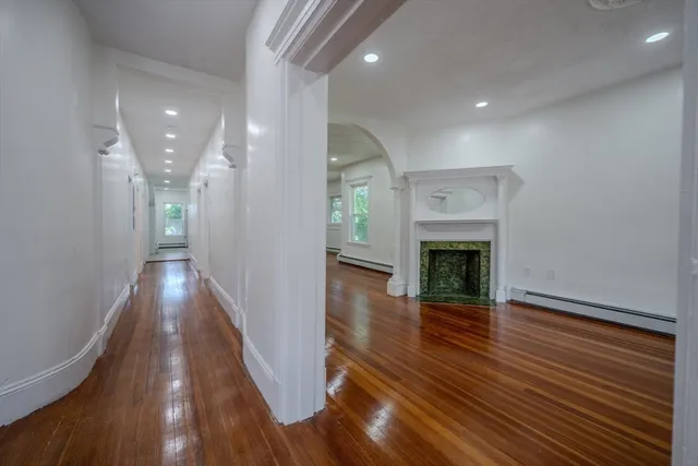 a view of an empty room with wooden floor fireplace and a window
