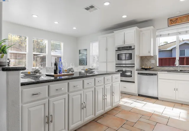 a kitchen with granite countertop white cabinets white appliances a sink and a window