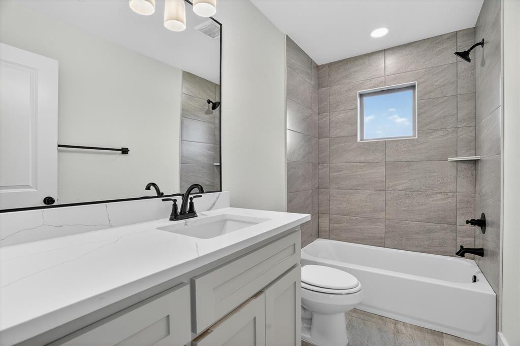 225 Kilkenny Road Poolville, TX 76487 - Photo 21 of 36 Bathroom featuring a vanity with a white countertop and undermount sink, a large mirror with a black frame, light gray shaker-style cabinetry, and a bathtub with gray tile surround and matte black fixtures
