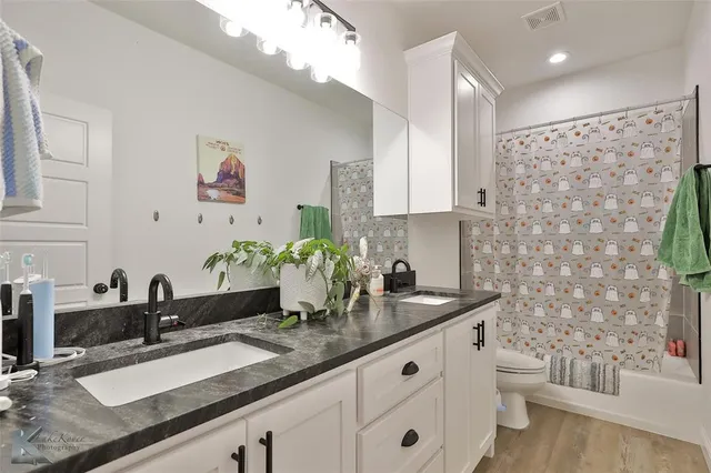 a bathroom with a granite countertop sink a toilet a mirror and shower