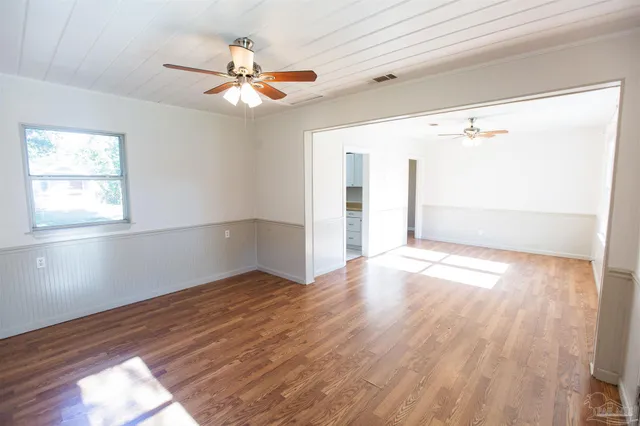 an empty room with wooden floor fan and windows