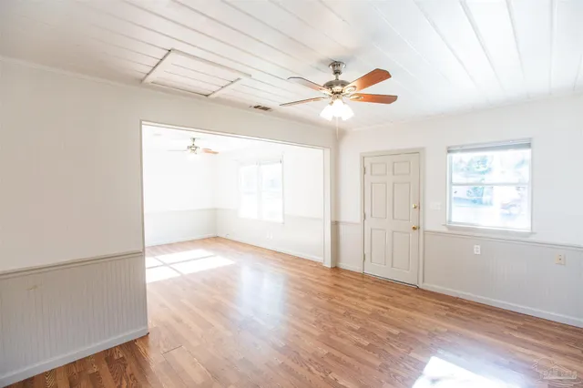 an empty room with wooden floor fan and windows