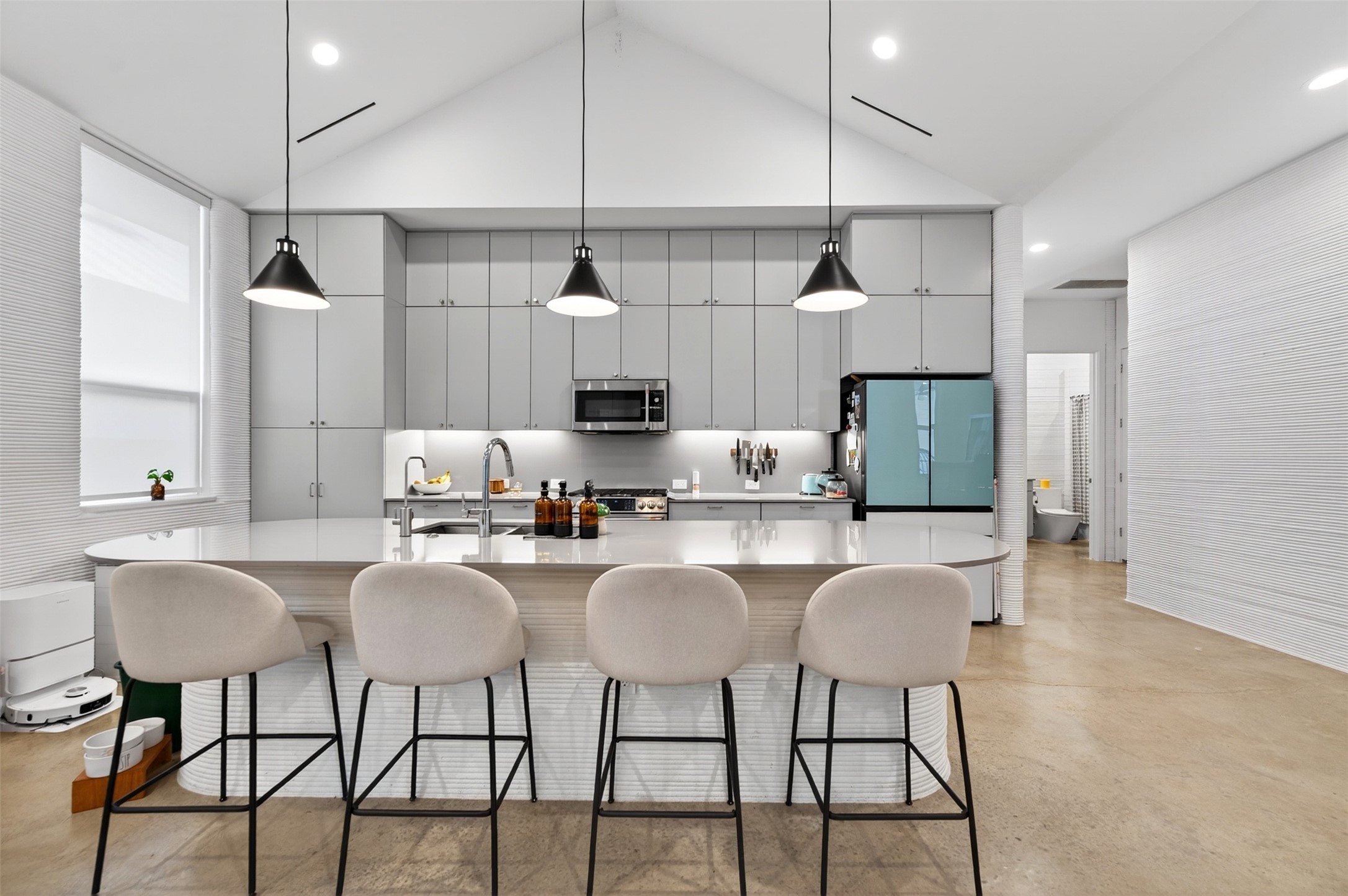 308 Painted Sunset Drive Georgetown, TX 78628 - Photo 9 of 26 Vaulted ceiling kitchen featuring a curved island with integrated seating, gray cabinetry, stainless steel appliances, and a unique textured wall finish