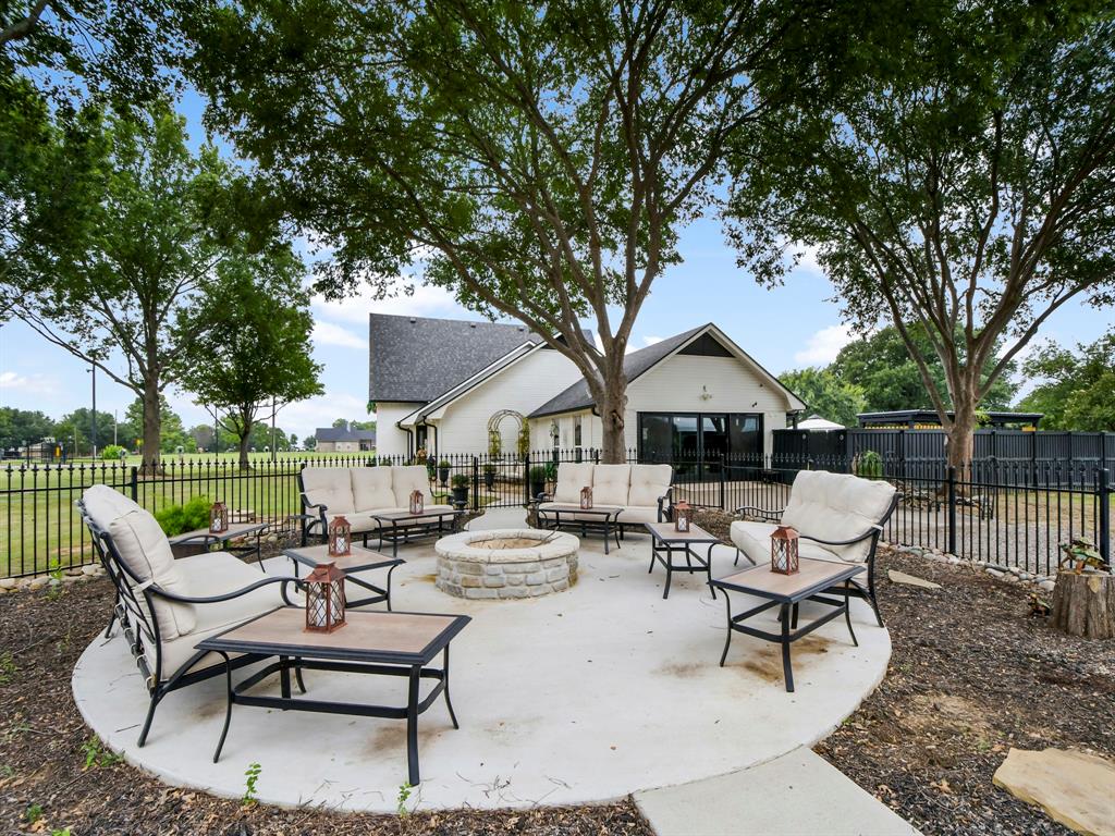 9867 Dripping Spring Road Denison, TX 75021 - Photo 4 of 40 Circular concrete patio featuring a stone-clad fire pit, mature trees, and a black wrought iron fence