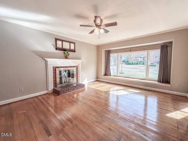 a view of an empty room with wooden floor fireplace and a window