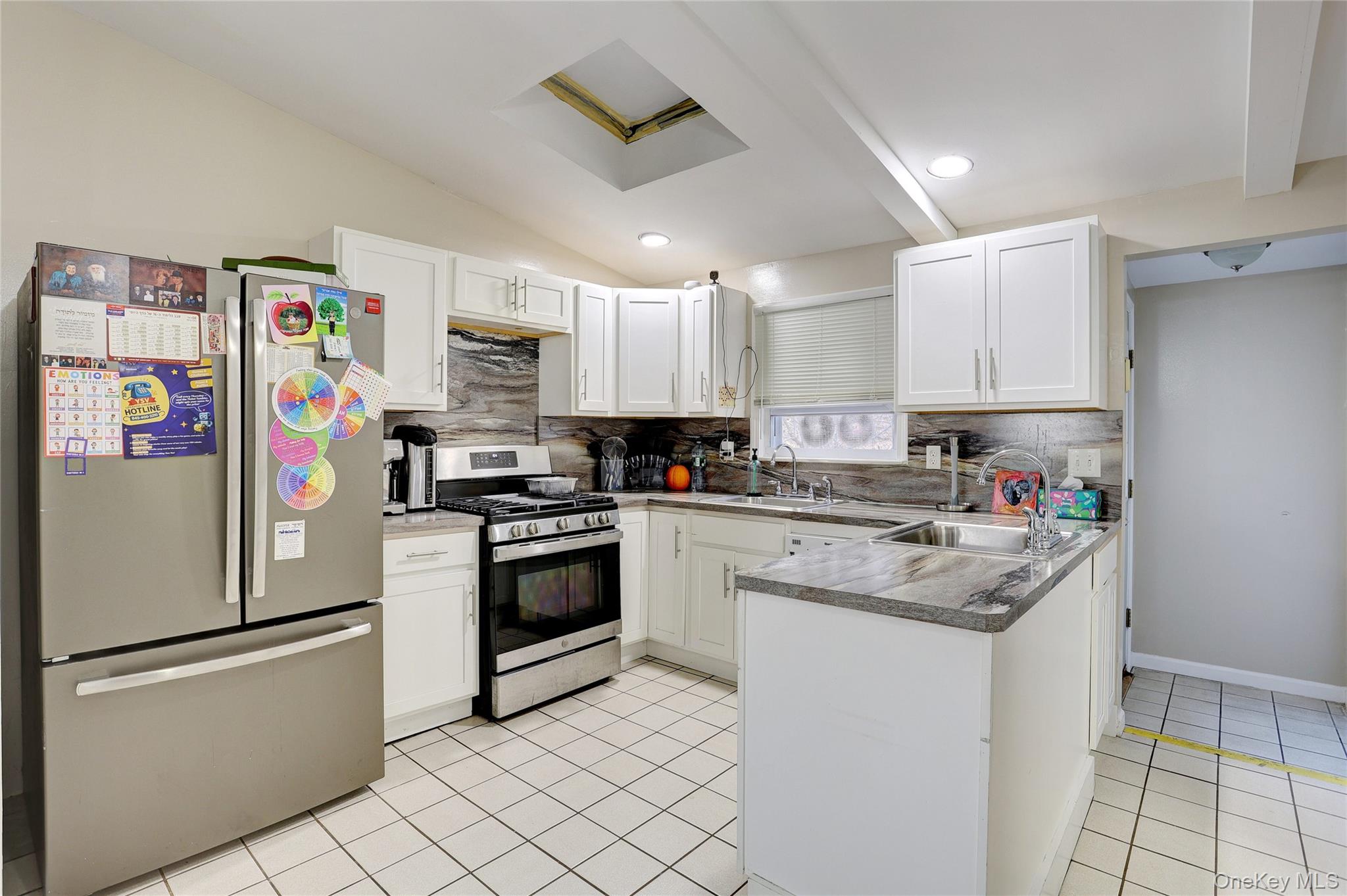 35 Regina Road Monsey, NY 10952 - Photo 11 of 34 Kitchen featuring appliances with stainless steel finishes, white cabinets, decorative backsplash, a peninsula, and light tile patterned floors