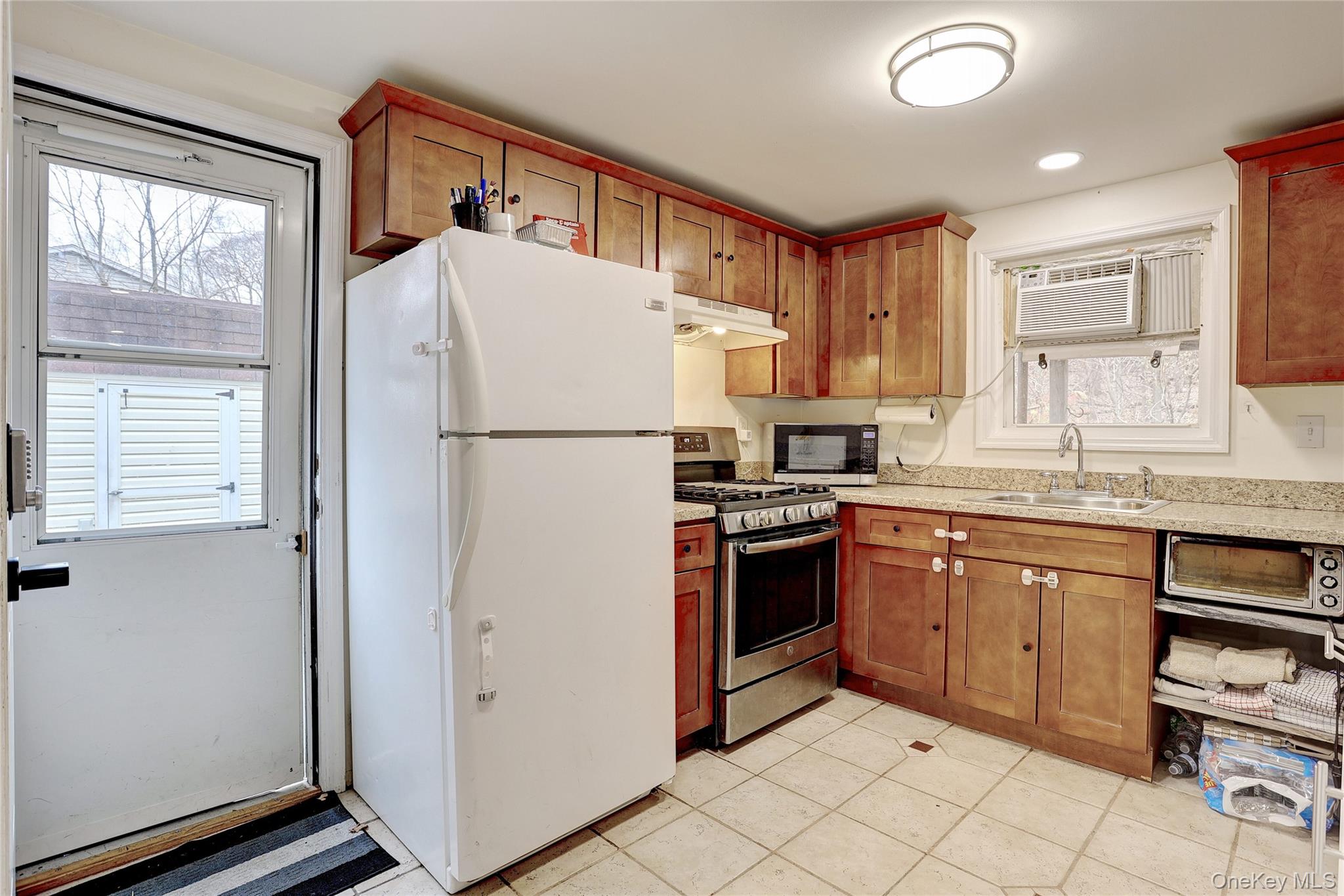 35 Regina Road Monsey, NY 10952 - Photo 23 of 34 Kitchen with freestanding refrigerator, gas stove, under cabinet range hood, brown cabinetry, and a wall unit AC