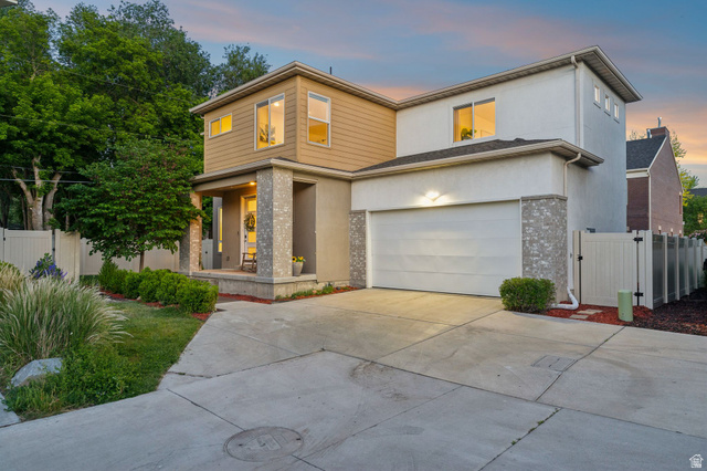 Modern architectural exterior featuring a two-car garage, covered porch with stone-clad columns, and a concrete driveway