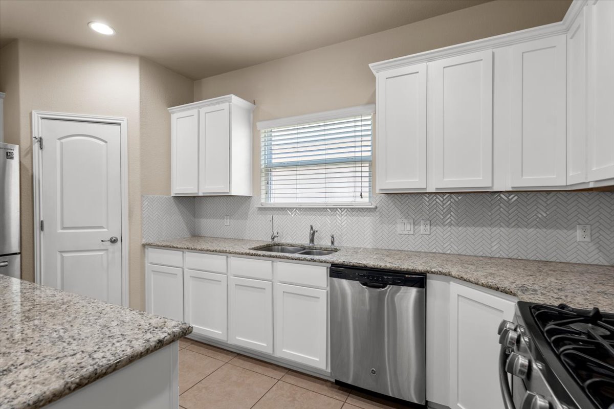 3451 Mayfield Ranch Boulevard, Unit 311 Round Rock, TX 78681 - Photo 10 of 40 Kitchen featuring white cabinetry, speckled countertops, a herringbone tile backsplash, and stainless steel appliances including a dishwasher and range