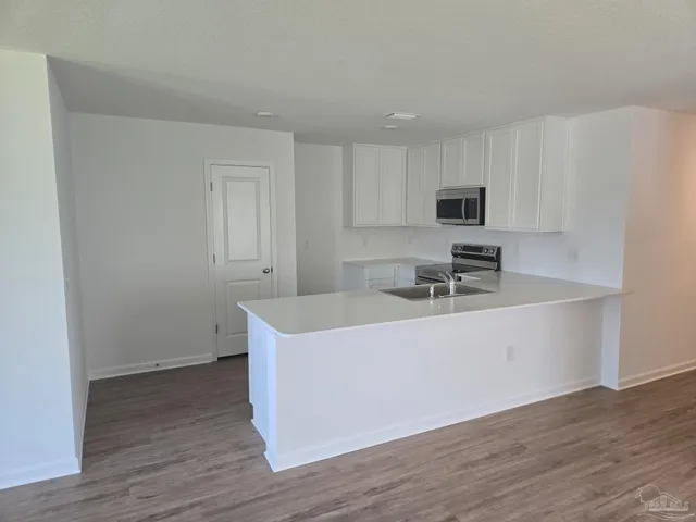 a white kitchen with wooden floor and stainless steel appliances