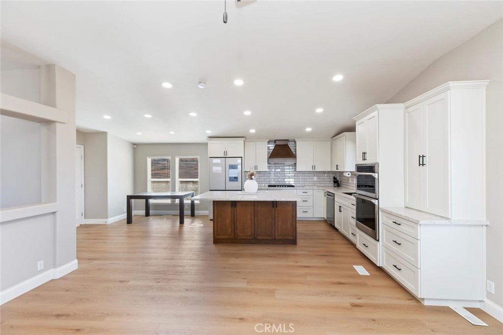 19310 Ann Way Perris, CA 92570 - Photo 16 of 75 a large white kitchen with kitchen island a stove a refrigerator a dining table and chairs with wooden floor