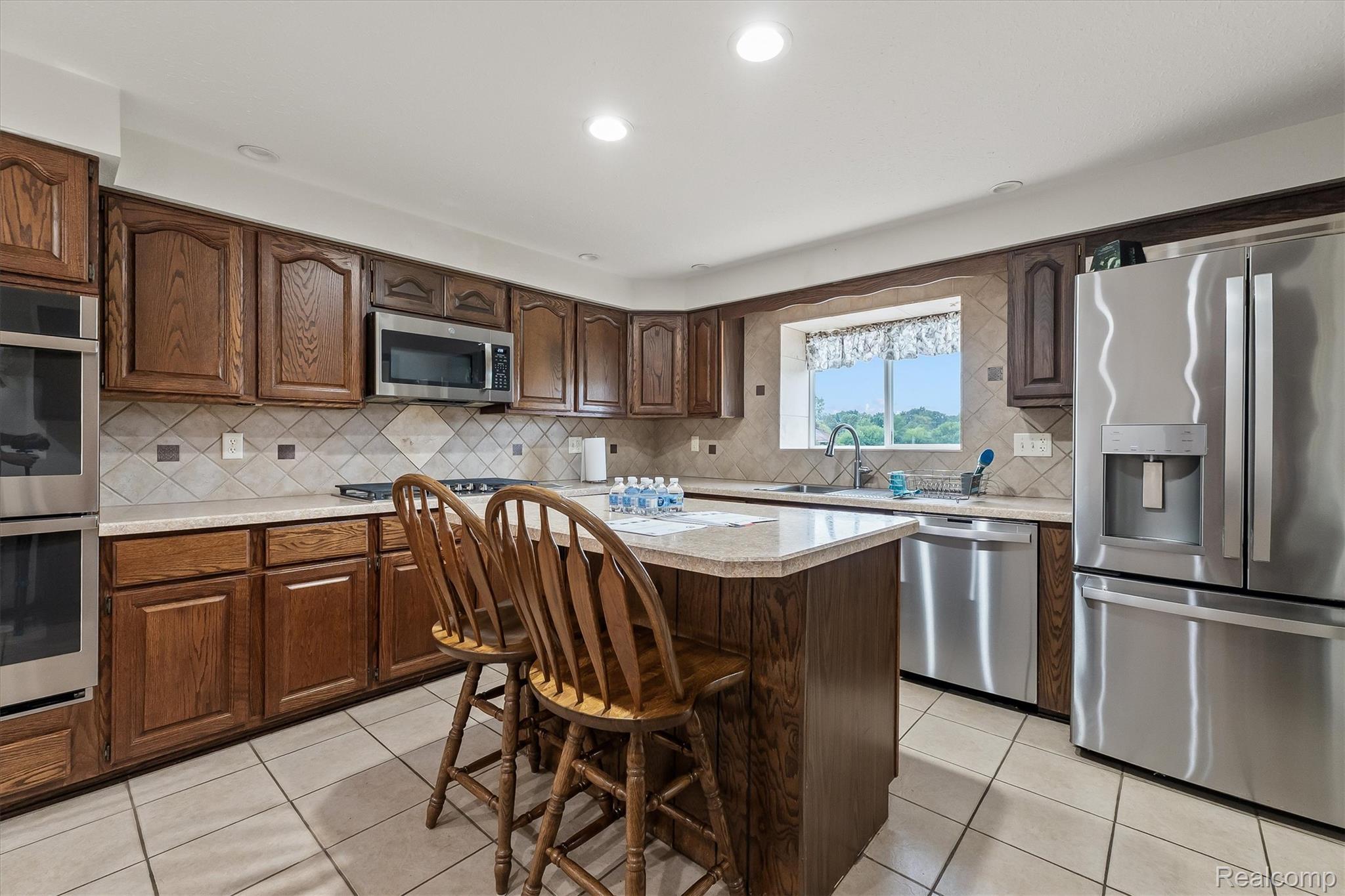 3553 North State Road Owosso, MI 48867 - Photo 12 of 45 Kitchen featuring wood cabinetry, stainless steel appliances, a center island with seating, tile backsplash, and light-toned countertops