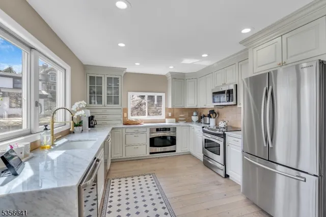 a large kitchen with a refrigerator a stove a sink dishwasher a oven with white cabinets and wooden floor