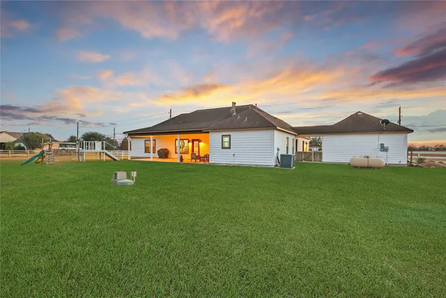 a view of a white house in front of a big yard with plants and large trees