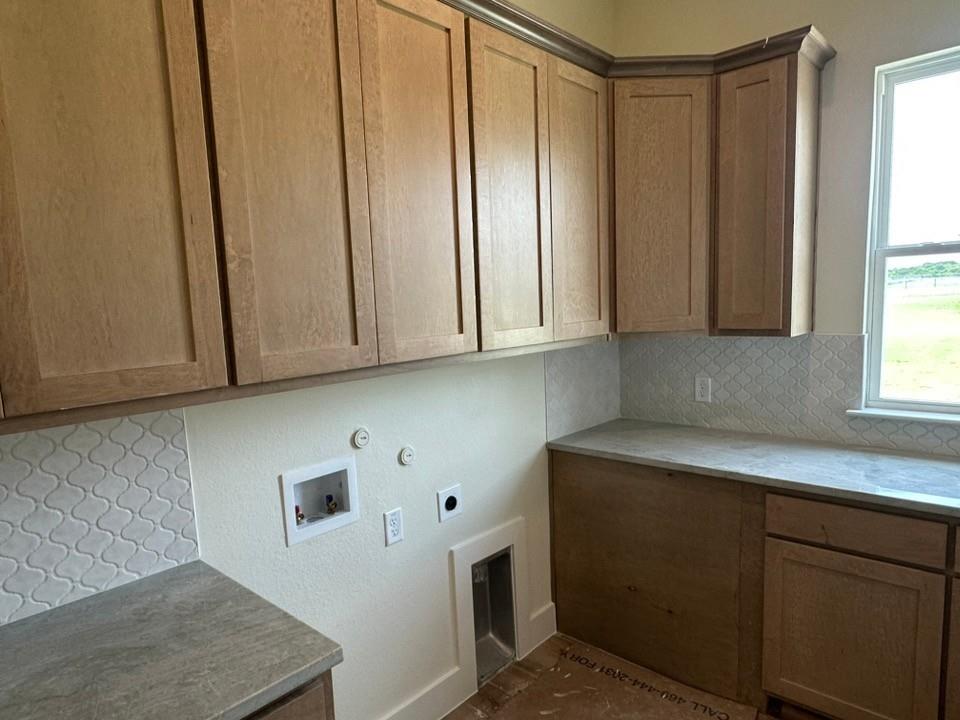 205 Cobb Road Leonard, TX 75452 - Photo 20 of 23 Utility room featuring upper and lower cabinetry with wood-finish doors, solid surface countertops, and a decorative tile backsplash