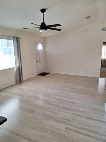 a view of an empty room with wooden floor ceiling fan