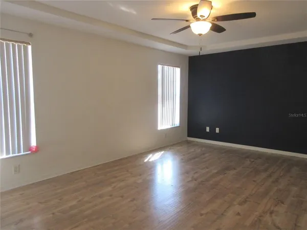 an empty room with wooden floor fan and windows