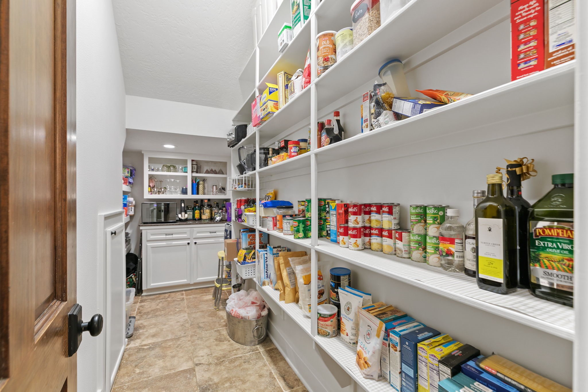 15601 Brown Road Tomball, TX 77377 - Photo 16 of 48 Wow! This spacious pantry features extensive shelving for storing your food, and a built-in cabinet counter space at the end, perfect for storage and organization. The room is well-lit with tile flooring, offering a practical and efficient space for kitchen essentials.