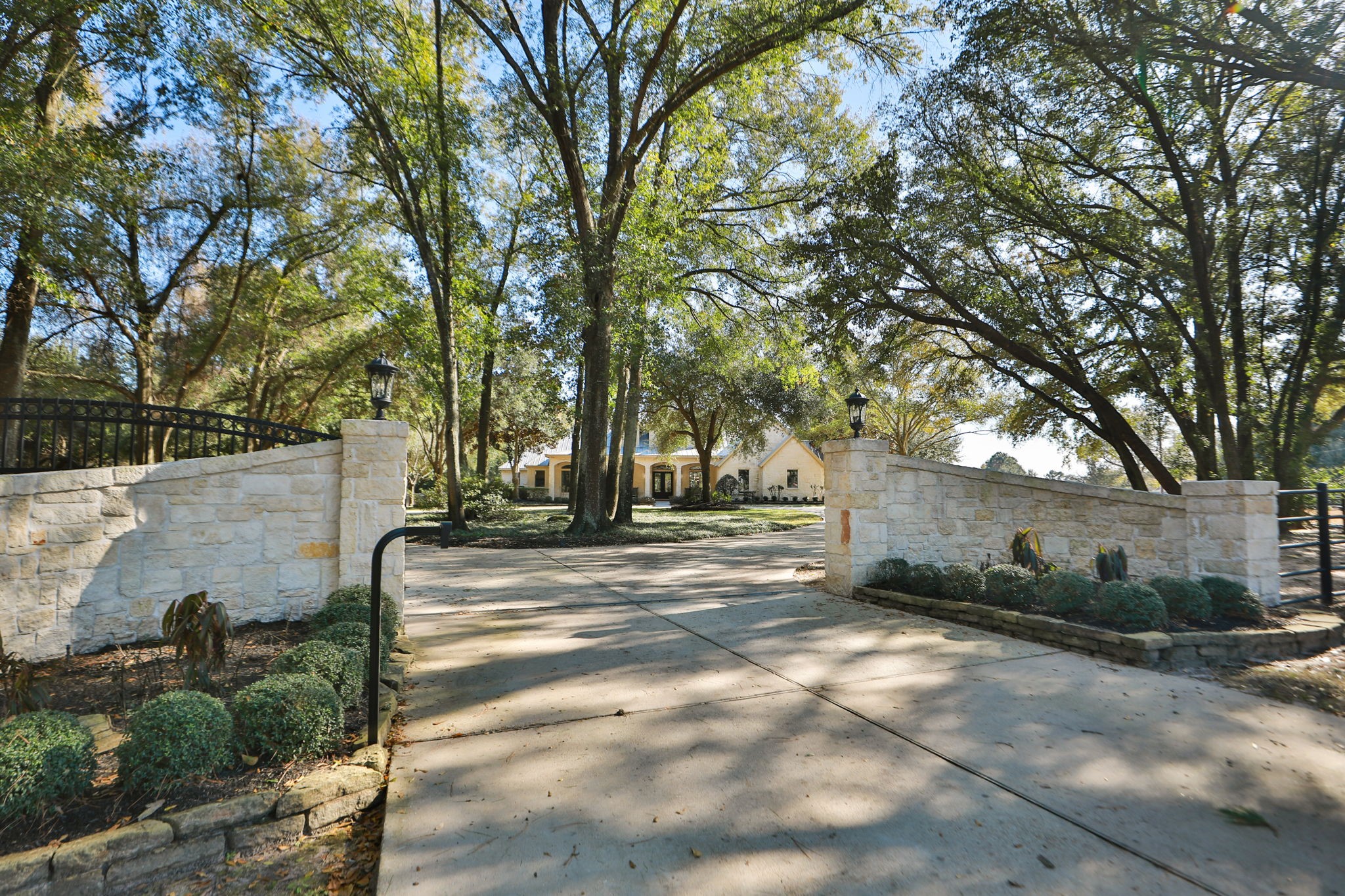15601 Brown Road Tomball, TX 77377 - Photo 2 of 48 Enjoy privacy with the gated entry and a picturesque driveway leading to a charming house, framed by mature trees and stone walls with lanterns. The setting provides a serene, private ambiance, perfect for a welcoming home.