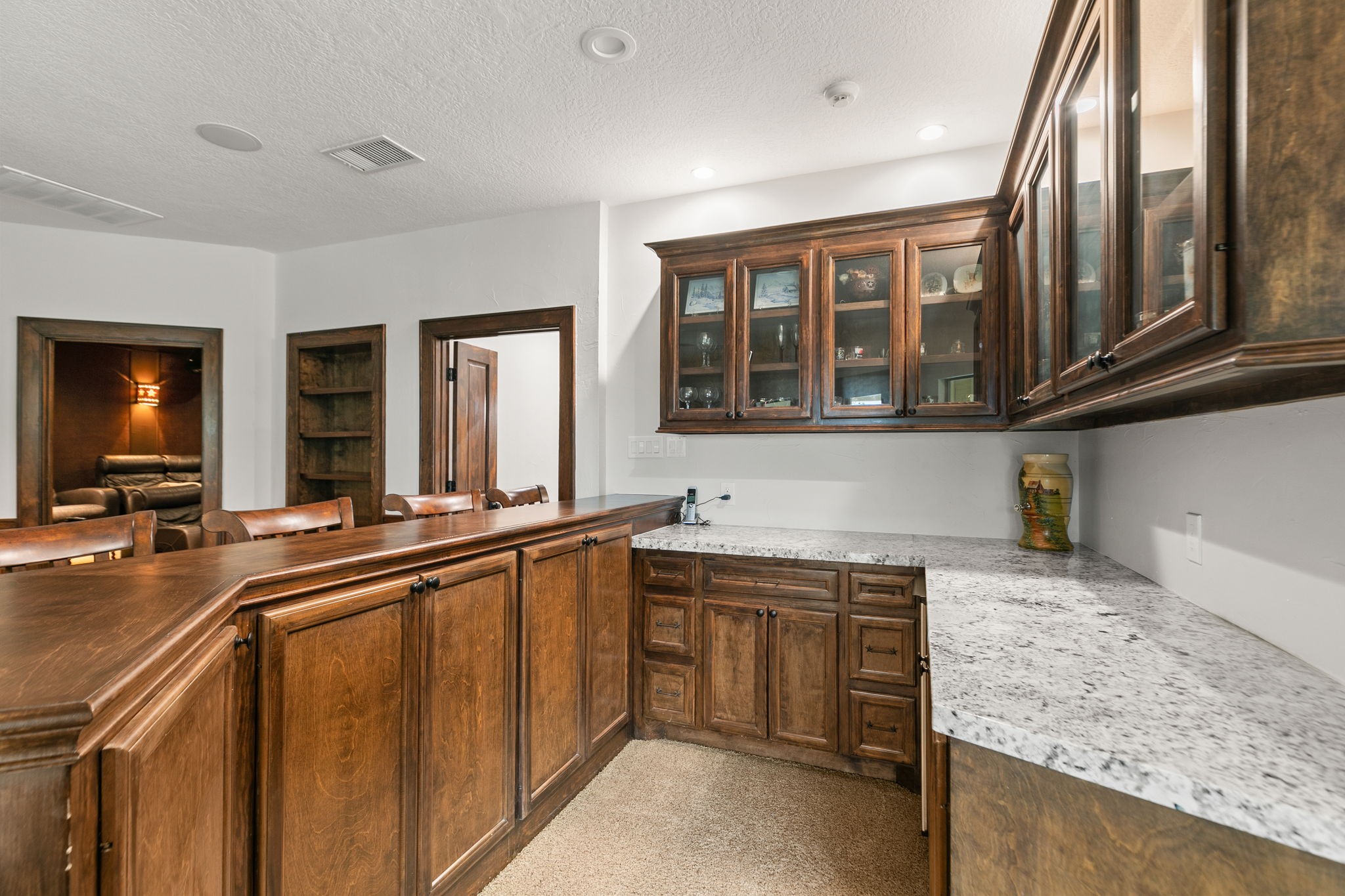 15601 Brown Road Tomball, TX 77377 - Photo 33 of 48 This photo showcases a cozy home bar area with rich wooden cabinetry, a granite countertop, and glass-front upper cabinets for displaying glassware. Bar seating for your bar stools. You will have fun entertaining your guests in this fabulous game room.