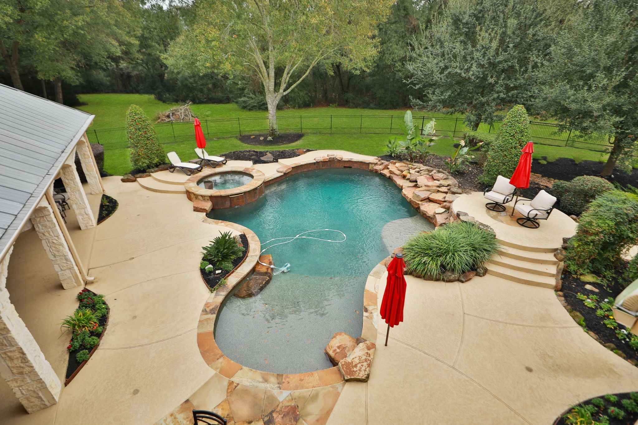 15601 Brown Road Tomball, TX 77377 - Photo 36 of 48 The backyard features a beautiful freeform pool with attached spa, surrounded by a spacious patio with plenty of room for your patio furniture. It's landscaped with lush greenery and overlooks a large, fenced lawn, offering a serene and private outdoor retreat.