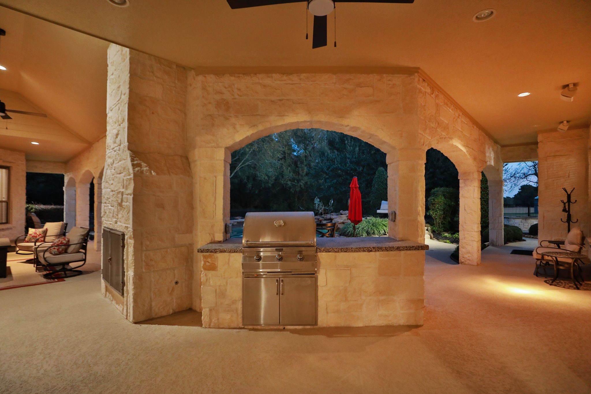 15601 Brown Road Tomball, TX 77377 - Photo 37 of 48 This sunset photo showcases a spacious outdoor living area with a built-in grill, stone accents, and archways. It features plenty of comfortable seating room and a view of a landscaped garden, perfect for entertaining and relaxation.
