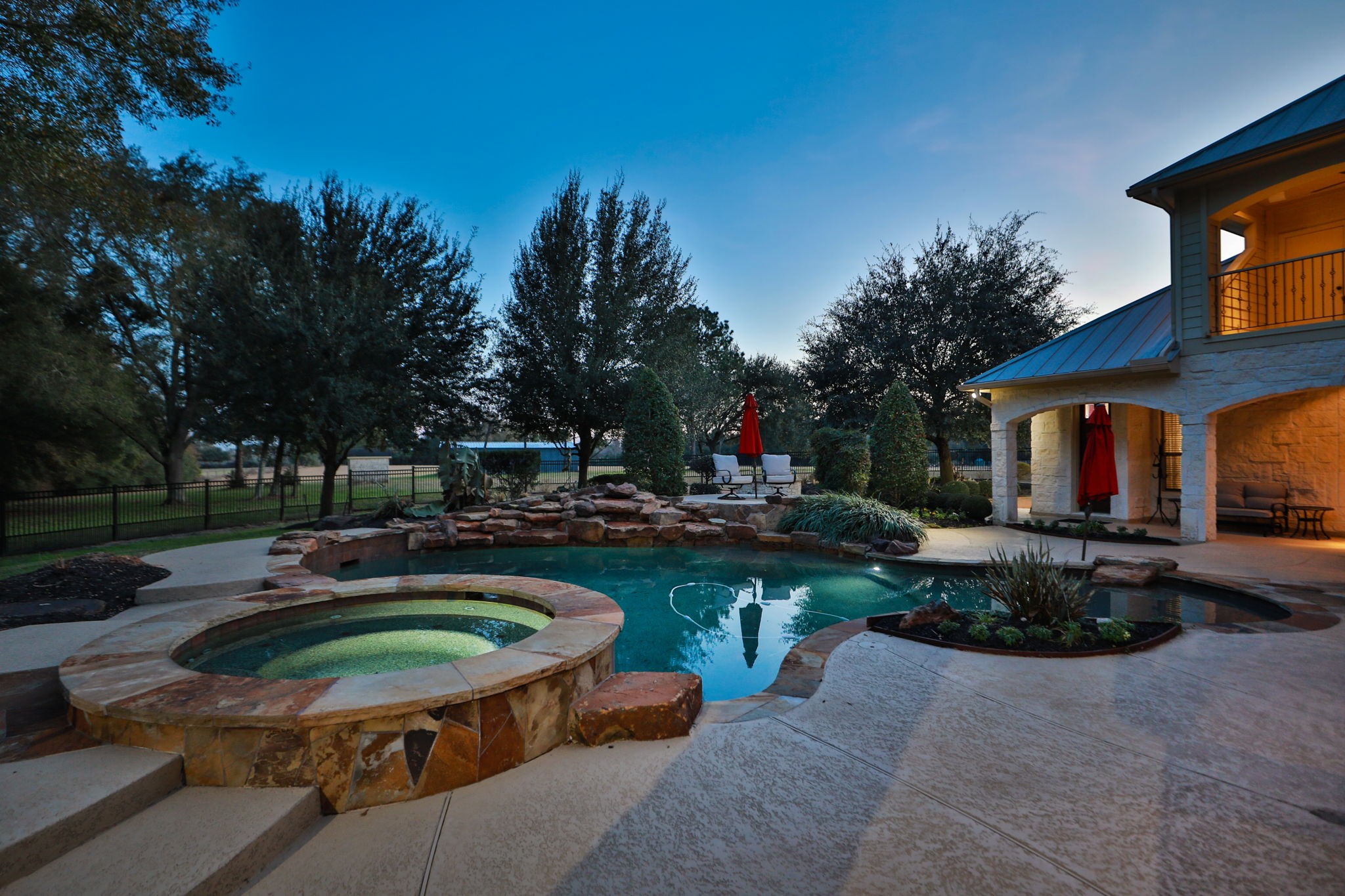 15601 Brown Road Tomball, TX 77377 - Photo 39 of 48 This sunset photo showcases a luxurious backyard featuring a stone-accented pool and hot tub, surrounded by lush landscaping and mature trees. Perfect for outdoor living and entertaining.
