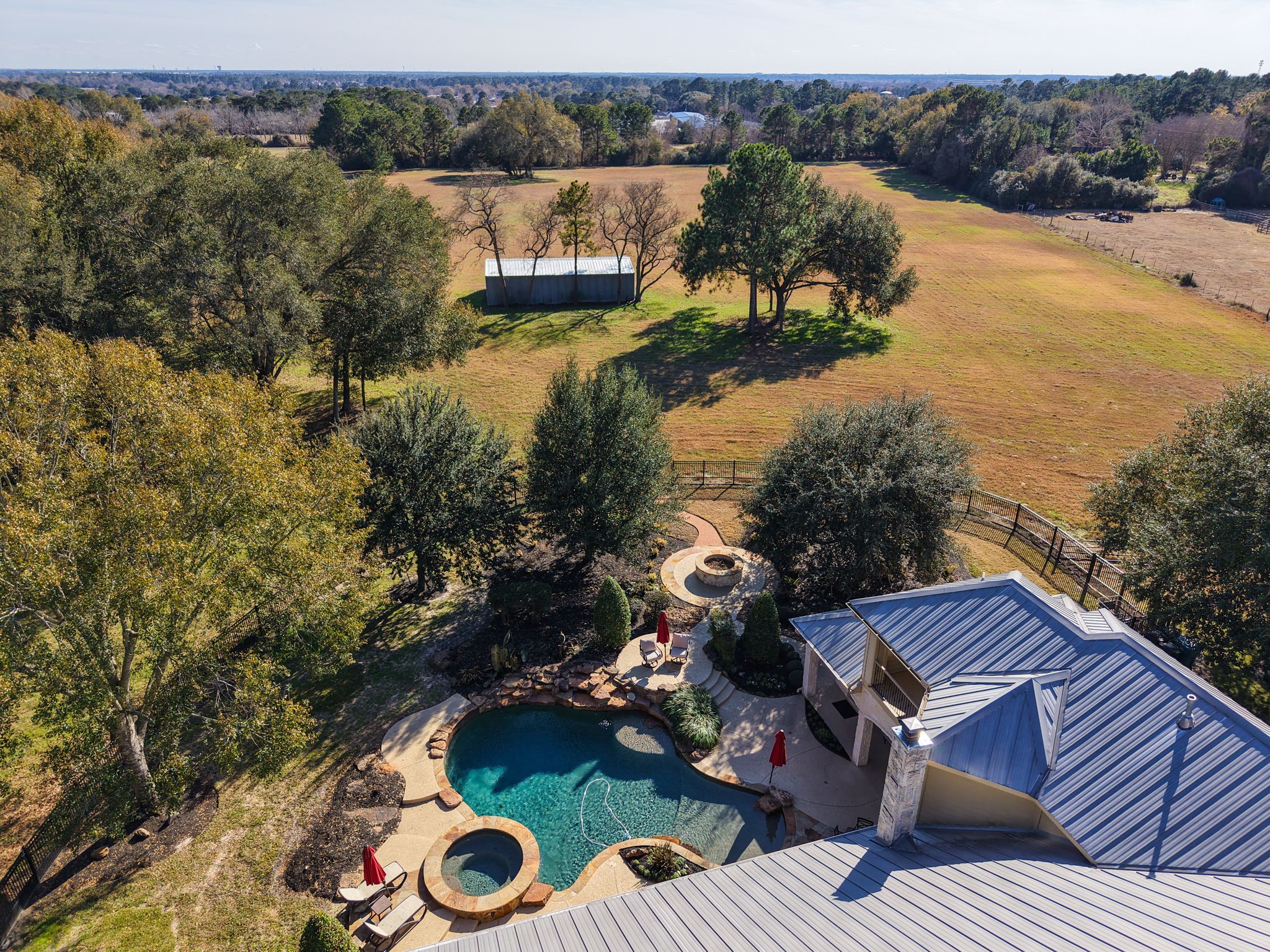 15601 Brown Road Tomball, TX 77377 - Photo 44 of 48 This aerial photo showcases a spacious property with a modern home featuring a metal roof, a beautifully landscaped pool, and a hot tub. The expansive backyard includes a fenced area and open fields, offering serene countryside views and plenty of outdoor space.