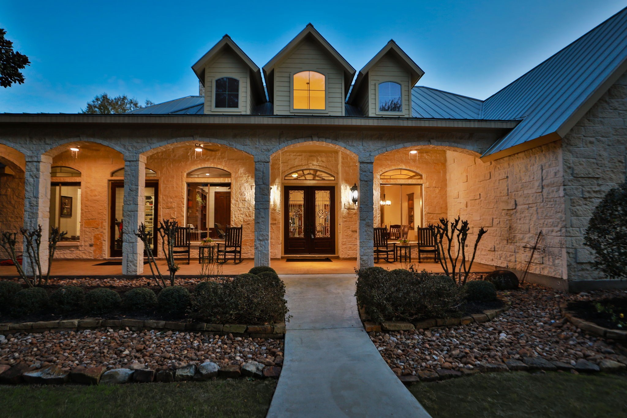 15601 Brown Road Tomball, TX 77377 - Photo 5 of 48 Stunning sunset photo with a spacious welcoming porch for your outdoor furniture, arched entryways, and beautiful stone exterior. The warm lighting and landscaped front yard create an inviting atmosphere.