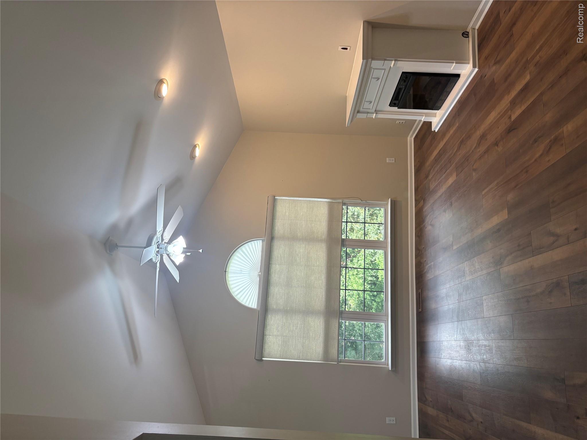 1859 Flagstone Circle Rochester, MI 48307 - Photo 2 of 8 Vaulted ceiling, wood-finish flooring, ceiling fan with integrated lighting, multiple windows with a half-round transom window, and a white mantel with an electric fireplace insert