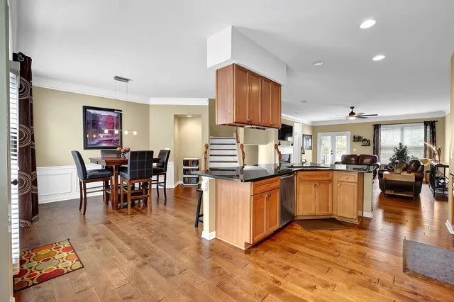 a kitchen with stainless steel appliances granite countertop a refrigerator a stove a sink a dining table and chairs with wooden floor