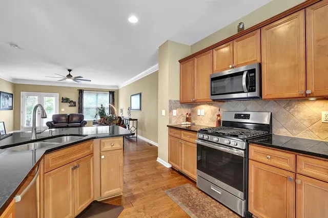 a large kitchen with stainless steel appliances granite countertop a stove top oven a sink dishwasher a dining table and chairs with wooden floor