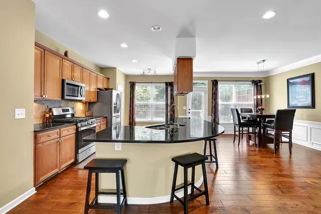 a open kitchen with stainless steel appliances granite countertop a stove top oven a dining table and chairs with wooden floor