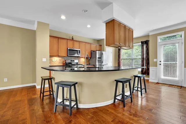 a kitchen with stainless steel appliances granite countertop a stove top oven a refrigerator a dining table and chairs with wooden floor