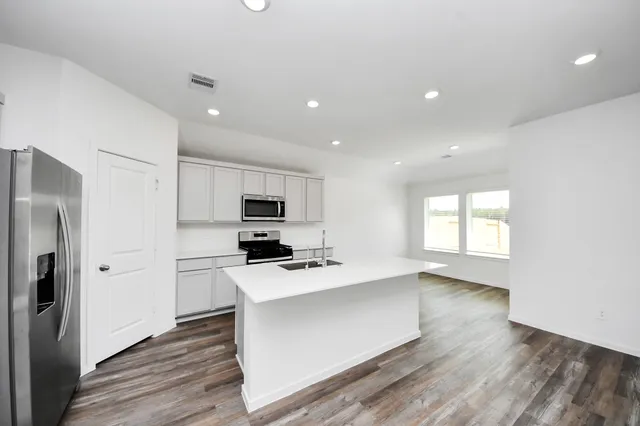 a kitchen with stainless steel appliances a refrigerator a stove a sink and white cabinets with wooden floor