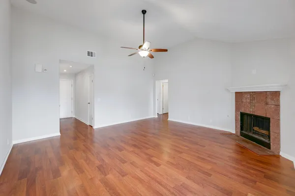a view of an empty room with wooden floor fireplace and a ceiling fan