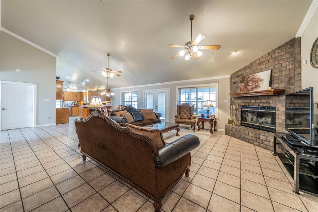 20175 Willow Glade Circle Pilot Point, TX 76258 - Photo 7 of 32 Living room with ceiling fan, a brick fireplace, lofted ceiling, light tile patterned flooring, and ornamental molding