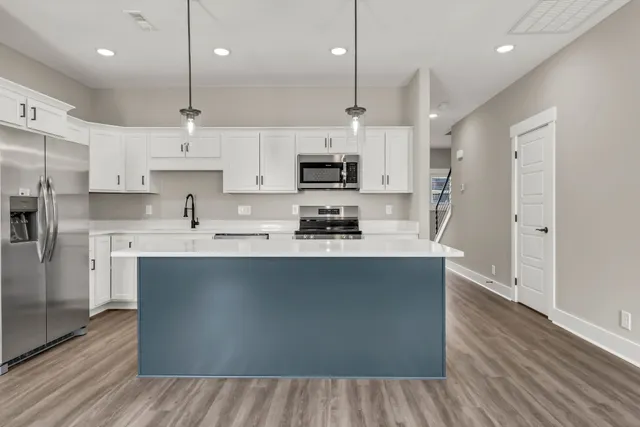 a kitchen with stainless steel appliances granite countertop a sink a stove a refrigerator and white cabinets with wooden floor