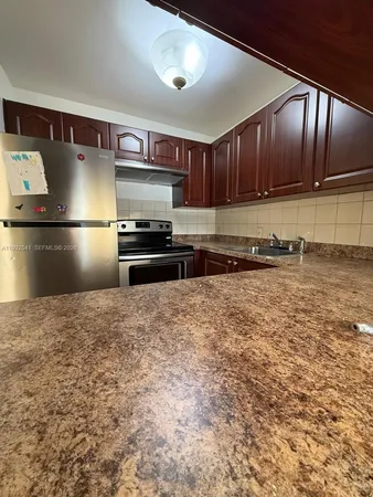 a kitchen with stainless steel appliances granite countertop a refrigerator a stove and a sink with wooden cabinets