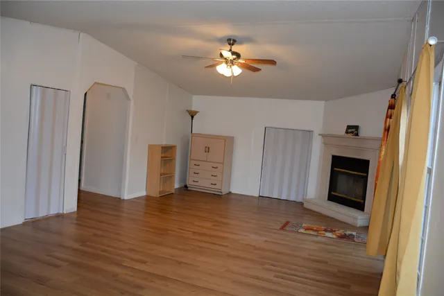 a view of an empty room with wooden floor fireplace and a window