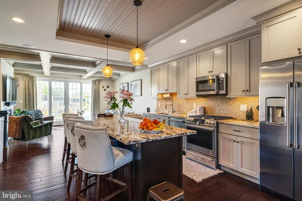 a kitchen with stainless steel appliances granite countertop a refrigerator a stove top oven a sink dishwasher a dining table and chairs with wooden floor