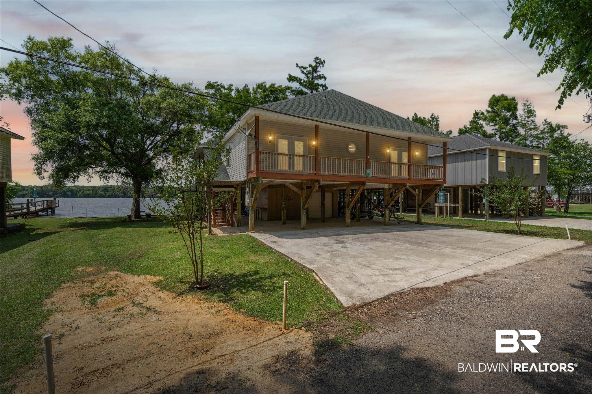 41923 Bayou Road Bay Minette, AL 36507 - Photo 1 of 35 Elevated coastal-style home featuring a covered front porch with white railing, a spacious concrete driveway, and a partially graveled front yard