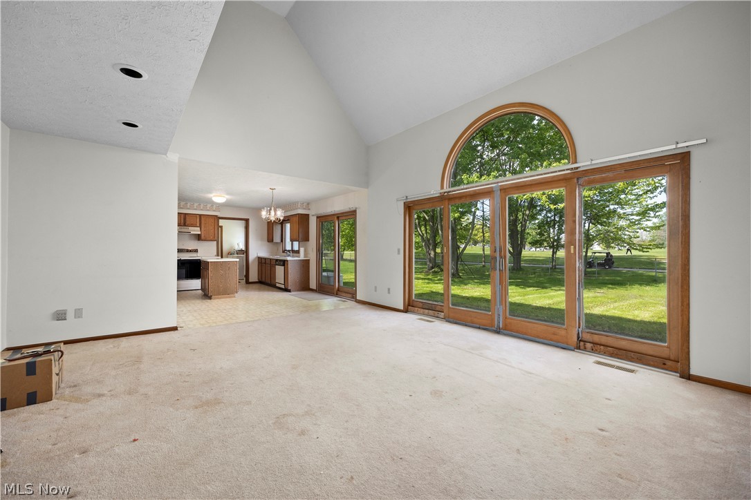 722 Jaycox Road Avon Lake, OH 44012 - Photo 2 of 48 Spacious living area featuring a vaulted ceiling with recessed lighting, large sliding glass doors, an arched transom window, and a partial view of the kitchen with wood cabinetry
