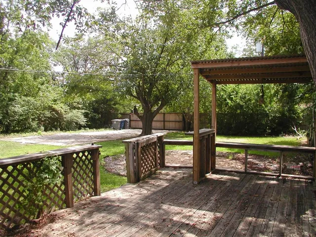 a view of a deck with a table and chairs under an umbrella with large trees