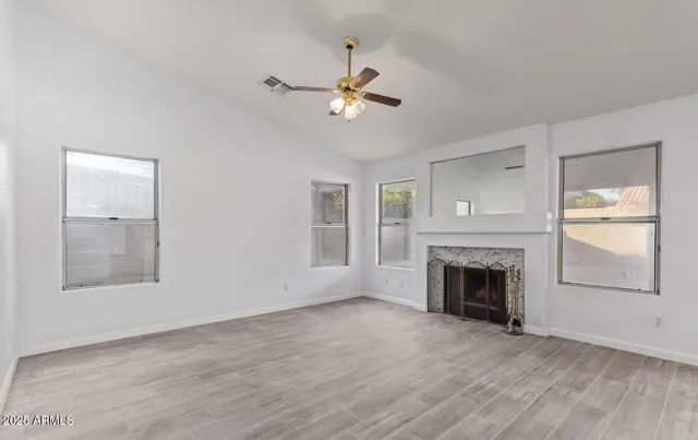 an empty room with wooden floor fireplace and windows