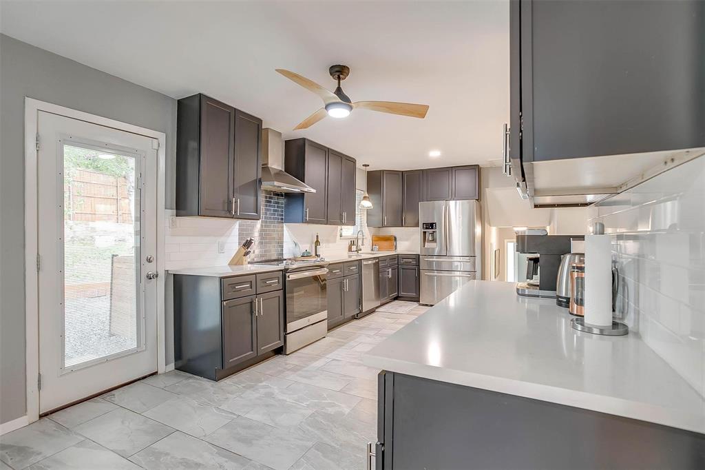 6609 Genoa Road Fort Worth, TX 76116 - Photo 11 of 39 Kitchen featuring appliances with stainless steel finishes, wall chimney range hood, a ceiling fan, decorative backsplash, and light countertops