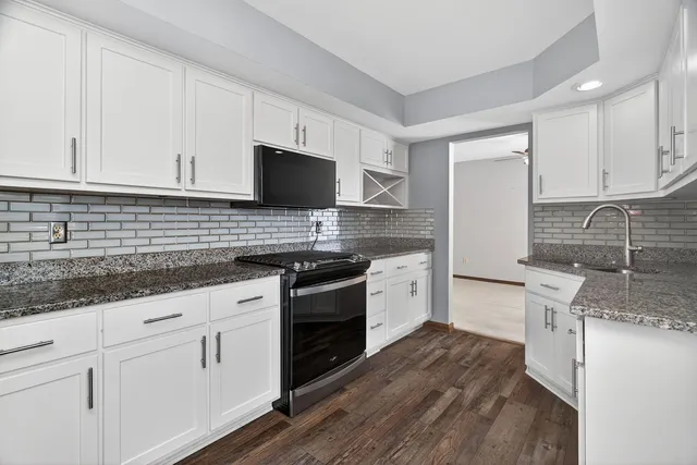 a kitchen with granite countertop a sink stainless steel appliances and white cabinets