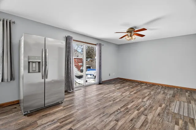 an empty room with wooden floor and way to kitchen