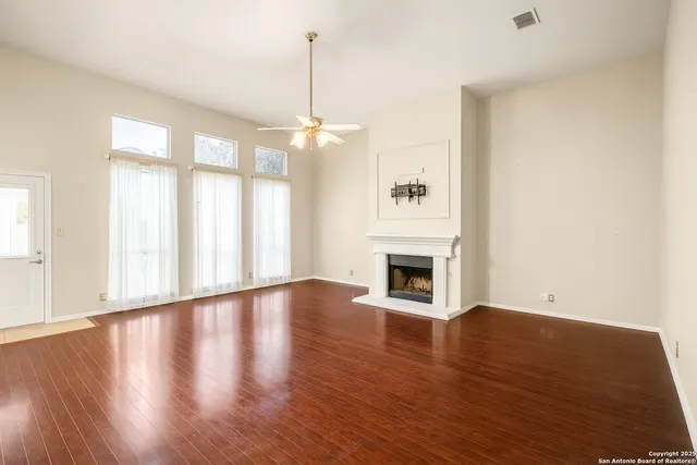 a view of an empty room with wooden floor fireplace and a window