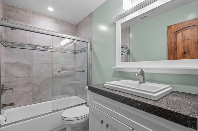 a bathroom with a granite countertop bathtub shower sink vanity and toilet